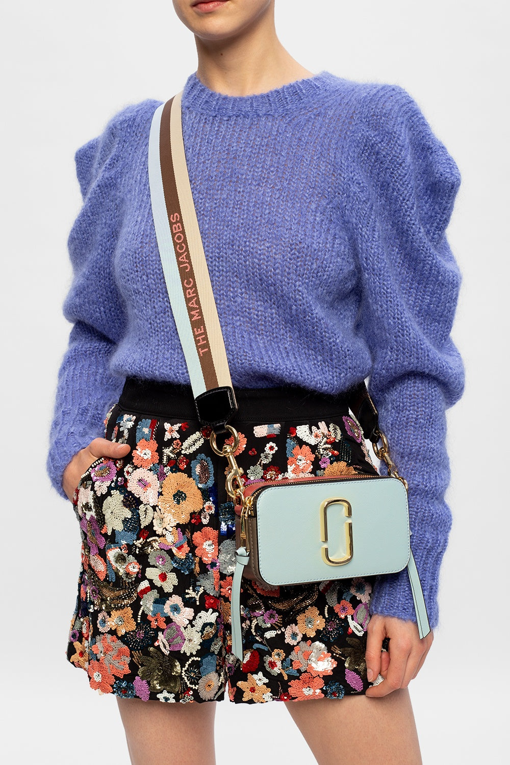 Person wearing a blue sweater and floral skirt with a light blue handbag on a white background